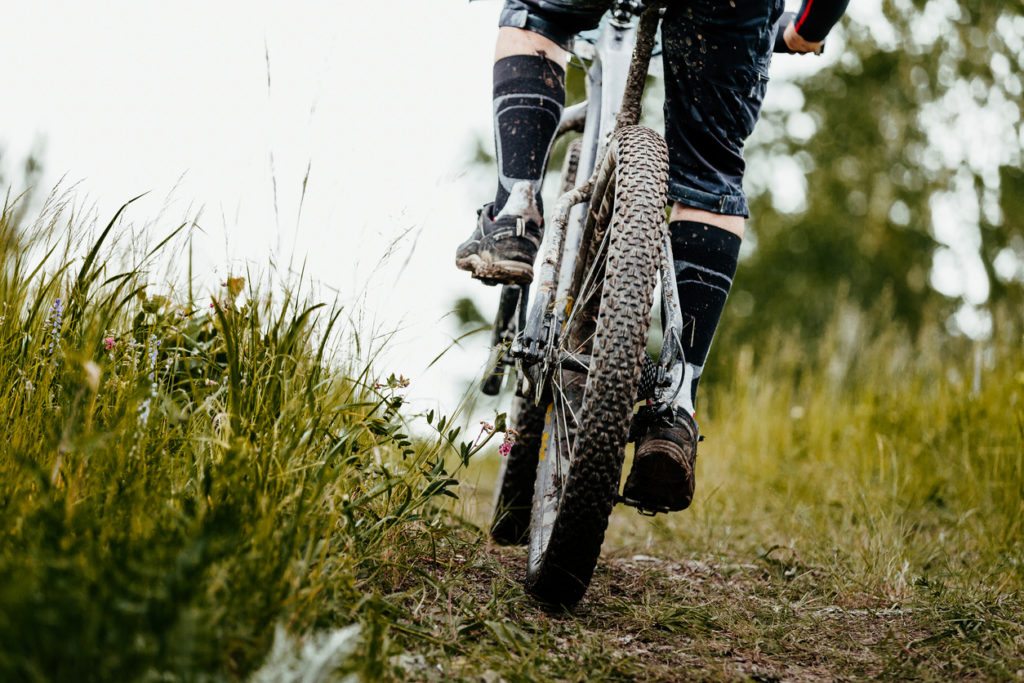 closeup mud mountain bike wheel and legs of cyclist